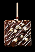 Chocolate-dipped treat with white drizzle and nuts on a stick against a black background