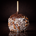 German chocolate gourmet caramel apple with coconut and pecans on a black background